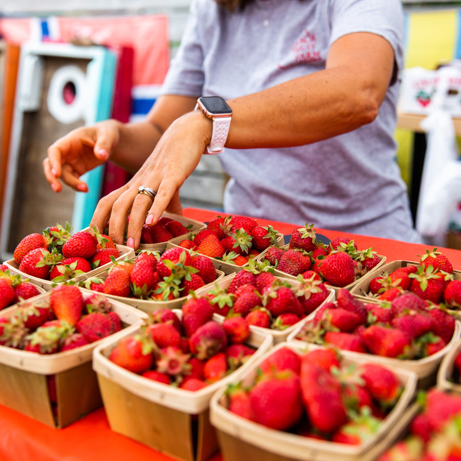 Hands picking up baskets of fresh strawberries