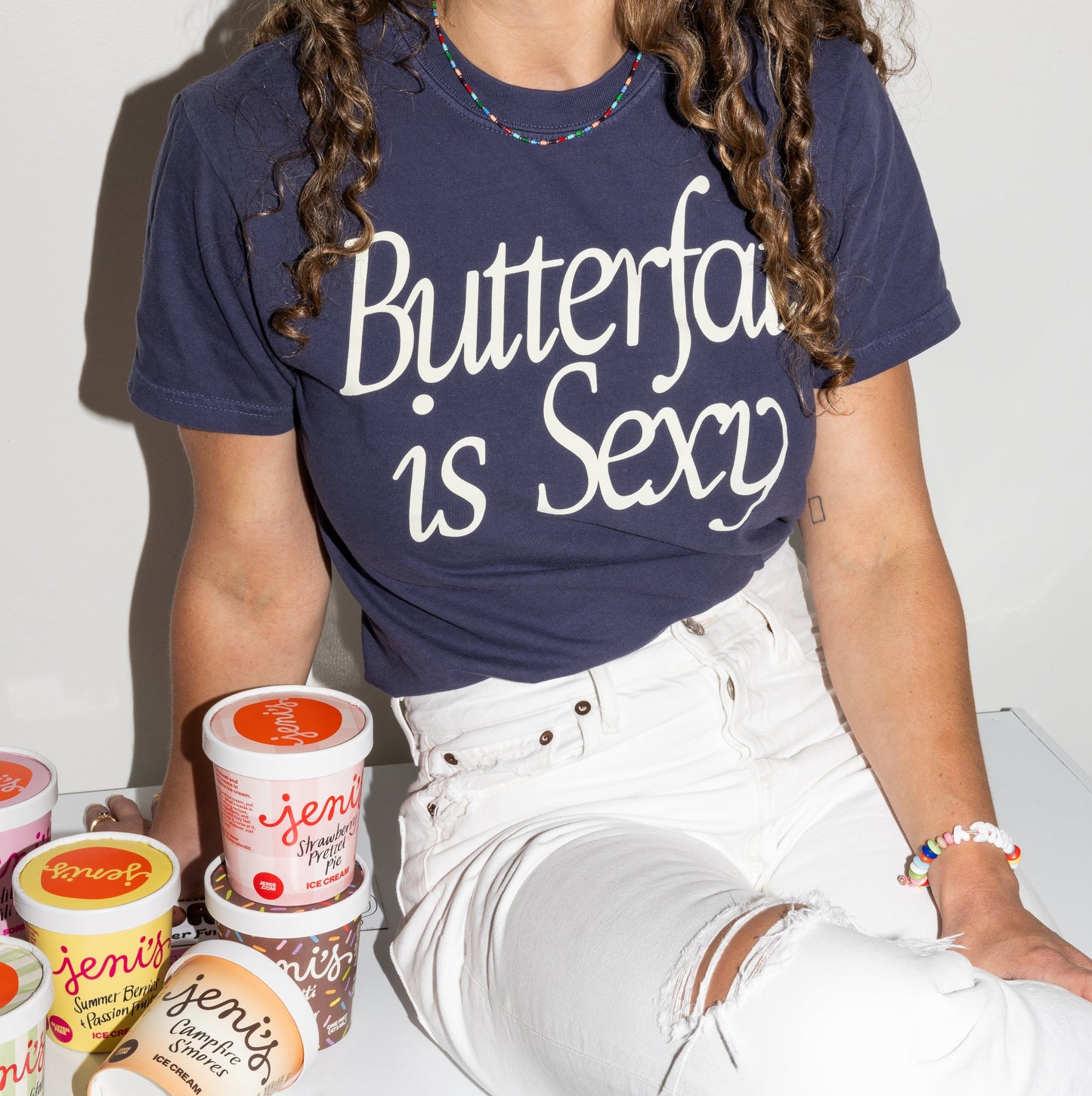 Person wearing a navy blue t-shirt with 'Butterfat is Sexy' text, sitting with Jeni's Ice Cream containers.