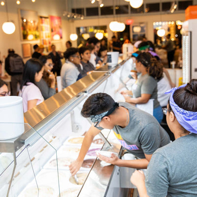 Employees at a Jeni's scoop shop scooping ice cream for customers.