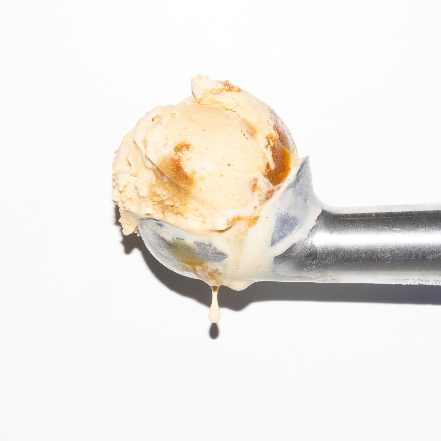A close-up of a metal ice cream scoop holding a scoop of ice cream with brown sugar blondie pieces, set against a plain white background.